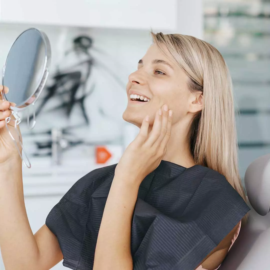 Happy female patient checking her smile after cosmetic gum treatment at Harmony Medical Center.